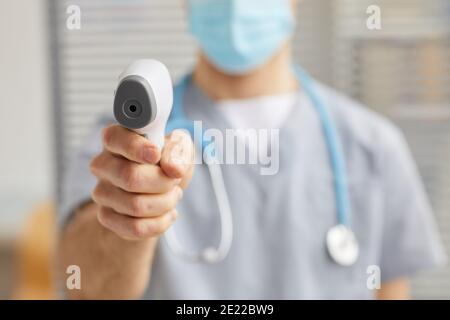 Gros plan d'un médecin masculin méconnaissable pointant le thermomètre infrarouge vers la caméra pendant le contrôle de la température à l'hôpital, copier l'espace Banque D'Images