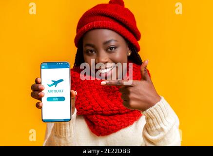 Gaieté Black Woman pointant vers un smartphone avec l'application Flight tickets À l'écran Banque D'Images