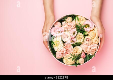 Fleuriste tenant un chapeau boîte ronde avec composition florale sur fond rose avec espace de copie. Boîte cadeau pour le 8 mars, Saint-Valentin, Fête des mères Banque D'Images