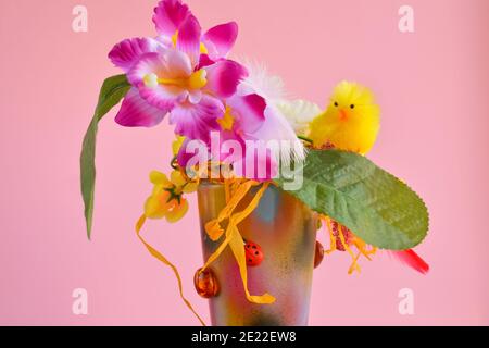 Composition de Pâques avec fleurs artificielles d'orchidées et une poussin jaune dans un pot en céramique sur fond rose, décoration de fête Banque D'Images