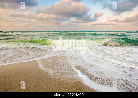 marée de mer sur un coucher de soleil nuageux. vagues vertes écrasant la plage de sable doré. temps d'orage à l'approche. concept de vacances d'été Banque D'Images