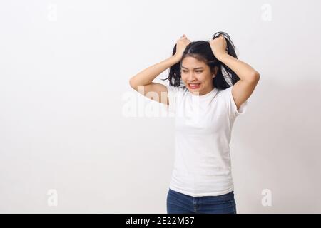 Portrait d'une jeune femme asiatique agacé en chemise blanche tirant ses cheveux et devenir folle. Isolé sur fond blanc avec espace de copie Banque D'Images