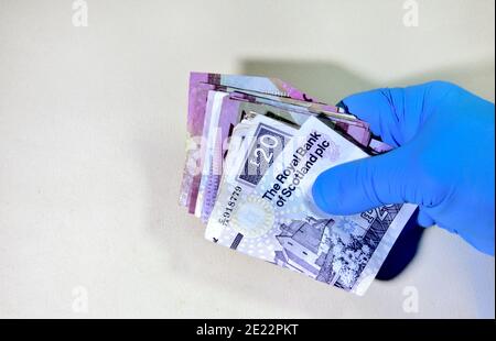 Main dans un gant de protection en caoutchouc tenant pile de billets de banque britannique, écossais, papier Banque D'Images