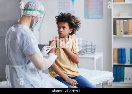 Portrait d'un adolescent afro-américain regardant une infirmière tenant une seringue pendant la vaccination contre le covid en clinique, espace copie Banque D'Images