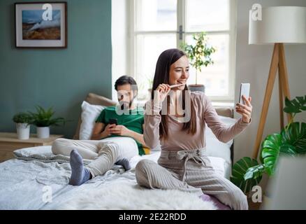 Jeune couple utilisant un smartphone sur le lit à l'intérieur à la maison. Banque D'Images