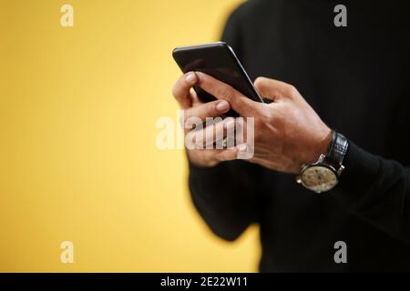Milieu de l'homme avec smartphone dans un studio sur fond jaune. Banque D'Images
