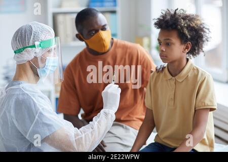 Portrait d'un adolescent effrayé regardant une seringue avec aiguille au cours de la vaccination contre le covid en clinique avec le père le soutenant Banque D'Images