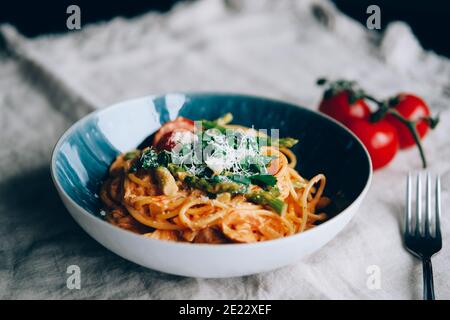 Pâtes avec asperges, sauce crémeuse à la tomate et au citron dans une assiette bleue. Banque D'Images