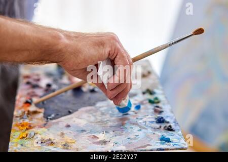 un artiste écourté non reconnaissable essorise la peinture d'un tube, allant mélanger les peintures pour le dessin Banque D'Images