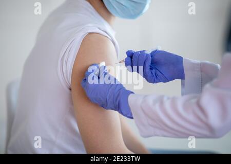 Vue en coupe d'un jeune homme recevant une injection du vaccin contre le coronavirus à la clinique, en gros plan Banque D'Images