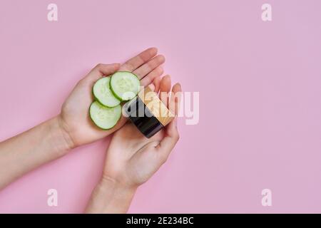 Mains de femme avec bouteille en verre, tranches de concombre sur fond rose Banque D'Images