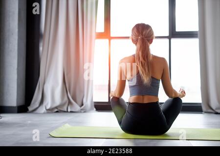 calme imreconnaissable femme assise dans lotus pose méditant seule dans studio lumineux, vue arrière Banque D'Images