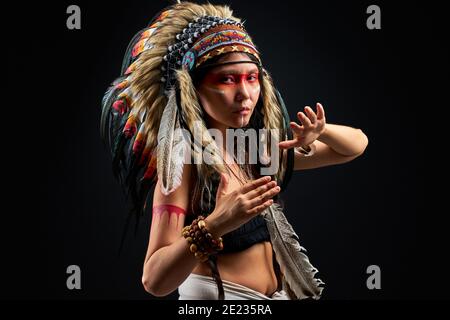 Modèle en port indien et maquillage coloré posant à la caméra, avec des plumes sur la tête. Tenue des peuples autochtones des Amériques, femme ethnique Banque D'Images