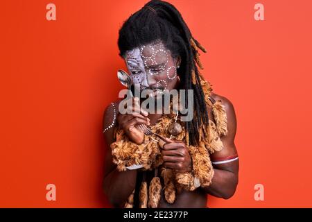 aborigen homme d'apparence africaine étudiant les couverts, regardant la cuillère avec intérêt, isolé sur fond rouge Banque D'Images