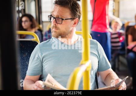 Un homme sérieux tient des journaux dans sa main tout en étant assis dans un bus. Banque D'Images