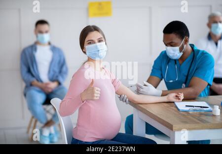 Femme enceinte recevant le vaccin contre le coronavirus à la clinique, montrant un geste de pouce vers le haut, recommandant l'immunisation Banque D'Images