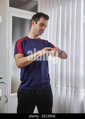 Cliché vertical d'un homme hispanique de belle taille dans le contrôle de vêtements de sport pouls après les exercices à la maison Banque D'Images