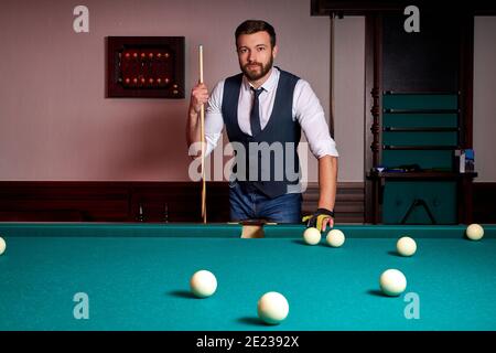 homme debout près de la table de billard, jouer au snooker, regarder la caméra, porter des vêtements formels, se reposer après le travail Banque D'Images