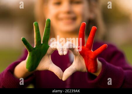 Forme de coeur des enfants peint à la main dans les couleurs de drapeau d'italie, langue du corps des enfants, concept d'amour des enfants. Cœur main sur la nature coucher de soleil arrière-plan bokeh Banque D'Images