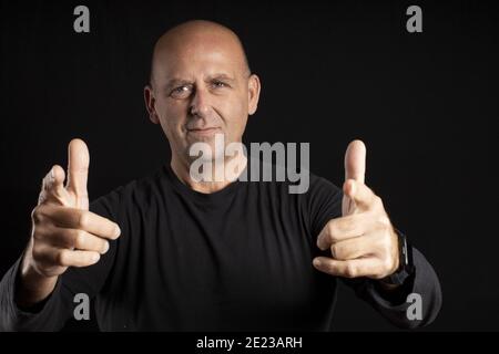 Homme chauve d'âge moyen avec des yeux lumineux pointant vers la caméra sur fond noir Banque D'Images