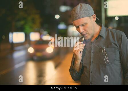 Homme mûr de fumer la cigarette électronique dans les rues la nuit Banque D'Images