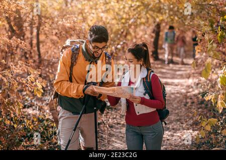 Randonneurs regardant la carte en se tenant dans les bois. En arrière-plan leurs amis. Saison d'automne, concept d'aventure. Banque D'Images