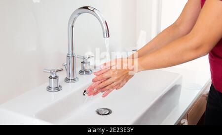 Femme se lavant les mains sous l'eau courante dans un lavabo blanc Banque D'Images