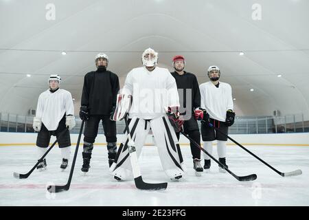 Plusieurs joueurs de hockey et leur entraîneur en uniforme sportif, gants, patins et casques debout sur une patinoire et en tenant des bâtons devant eux Banque D'Images