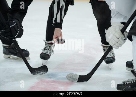 Main de l'arbitre tenant le palet sur la patinoire avec deux joueurs de hockey avec des bâtons debout autour de lui et attendant c'est le moment de le photographier Banque D'Images