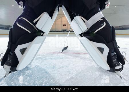 Vue arrière des jambes du joueur de hockey sur patins debout sur la patinoire et le bâton de maintien devant lui lors de la préparation de la prise de vue Banque D'Images