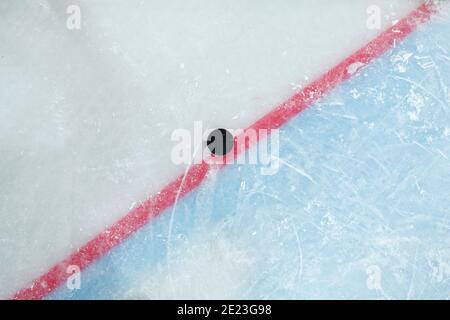 Palet se trouvant sur une ligne rouge séparant l'espace de jeu et la zone de filet sur la patinoire pour jouer au hockey qui peut être utilisé comme arrière-plan Banque D'Images