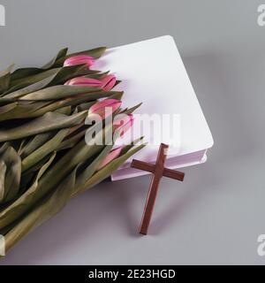 Croix en bois, bible et fleurs de tulipe de printemps fraîches. Temps de résurrection. Concept d'église.vue de dessus. Espace de copie. Banque D'Images