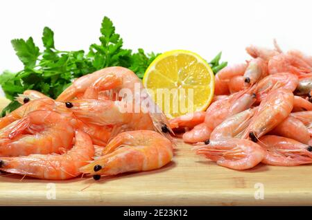 Crevettes bouillies avec citron et herbes fraîches sur un bois planche à découper sur fond blanc Banque D'Images