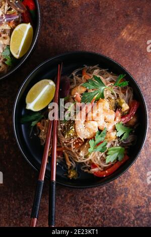 Remuez les nouilles frites avec les crevettes et les légumes dans un wok sur une table sombre, vue du dessus Banque D'Images