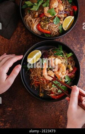Remuez les nouilles frites avec les crevettes et les légumes dans un wok sur une table sombre, vue du dessus Banque D'Images