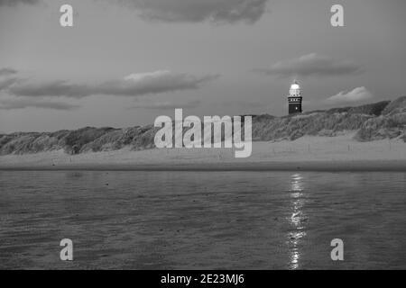 Le phare noir et blanc se trouve sur la côte hollandaise avec un ciel spectaculaire et coloré de crépuscule ou d'aube derrière lui. Photo monochrome de haute qualité Banque D'Images