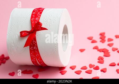 Rouleau de papier toilette en cadeau pour la Saint-Valentin, à côté de coeurs rouges sur fond rose. Copier l'espace Banque D'Images