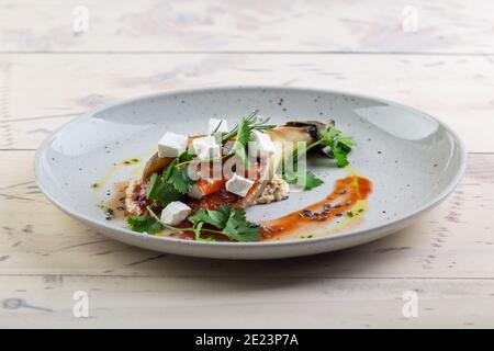 Aubergines cuites au four, juteuses et appétissantes, avec tomates et herbes sur une assiette blanche servie dans un restaurant Banque D'Images