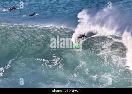 Vue à distance d'un surfeur méconnaissable sur une vague extrême. Banque D'Images