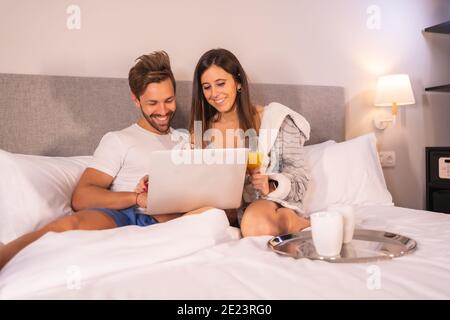 Couple aimant heureux se détendre dans la chambre à coucher et en utilisant un ordinateur portable Banque D'Images