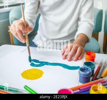 L'enfant tire le soleil et la mer dans la gouache sur une feuille de papier blanche. Enseignement à domicile. Formation de dessin. L'indépendance de l'art des enfants Banque D'Images