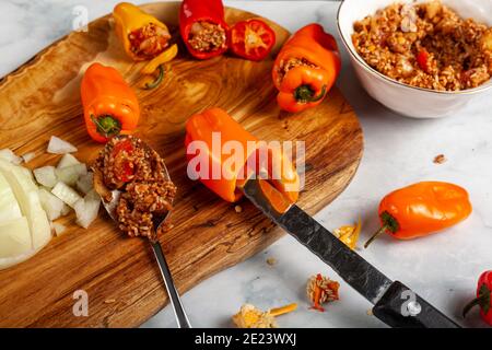 Fabrication de poivrons farcis à l'aide de poivrons rouges et jaunes colorés avec des graines retirées avec un couteau et garniture faite de riz, viande, oignon en dés, Banque D'Images