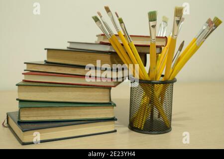 Pile de livres avec quelques pinceaux de peinture sur le côté un bureau en bois Banque D'Images