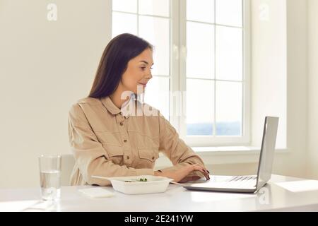 Bonne femme assise à la réception, déjeuner à emporter et navigation sur le site Web de livraison de repas Banque D'Images