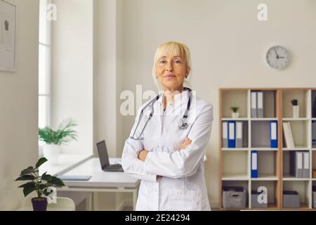 Positive confiante femme médecin âgé en uniforme debout et regardant à l'appareil photo Banque D'Images