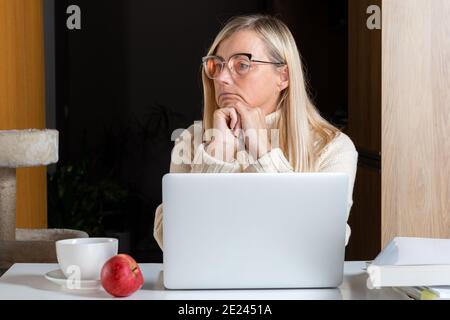 femme assise à un ordinateur portable dans un bureau à la maison et regardant attentivement dans la distance, femme réfléchie prendre une pause de travail Banque D'Images