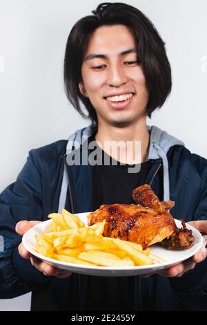 Cliché vertical d'un homme hispanique heureux avec deux mains contenant une assiette de poulet frit et de pommes de terre Banque D'Images