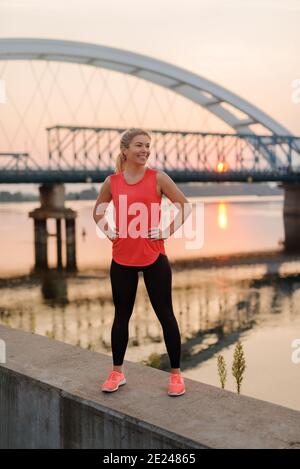 Une fille blonde sportive et sûre, debout près de la rivière après l'entraînement. Vue sur l'extérieur. Banque D'Images