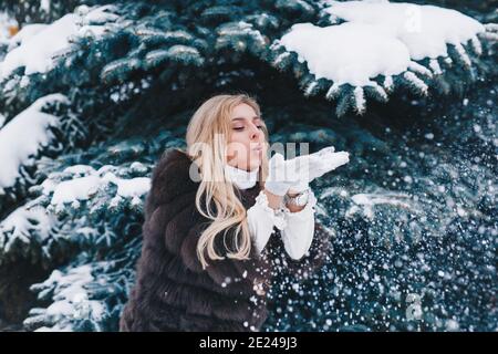 Belle fille d'hiver soufflant de la neige dans le parc gelé en hiver jour Banque D'Images