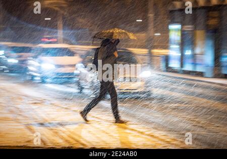 12 janvier 2021, Hessen, Francfort-sur-le-main: Un homme avec un parapluie et une protection de bouche-nez traverse une rue dans le centre-ville pendant l'heure de pointe du matin en conduisant de la neige. En Hesse, des routes glissantes doivent être attendues, même à basse altitude. Photo: Frank Rumpenhorst/dpa Banque D'Images